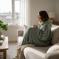 Oversized cozy hoodie in sage green styled on a woman relaxing at home on a neutral linen sofa